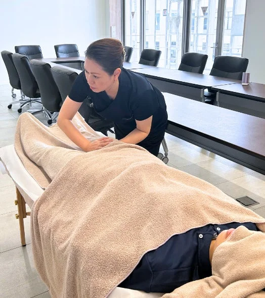 オフィスのような場所で、施術者がマッサージテーブルに横たわる利用者に施術を行っている様子