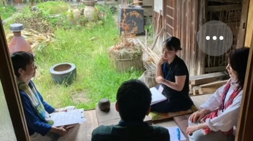 縁側のような場所で数人の男女が書類を手に話し合っている様子