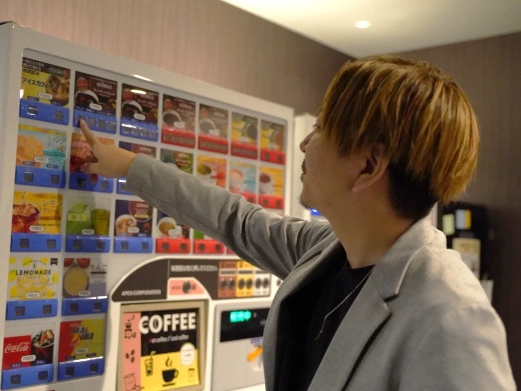 男性が自販機で飲み物を選んでいる様子