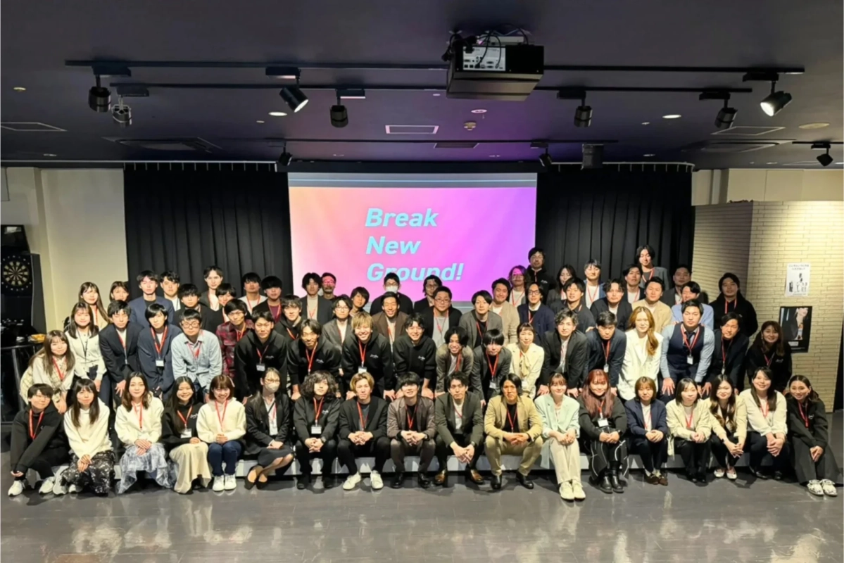 「Break New Ground!」と表示されたスクリーンを背景に集合写真