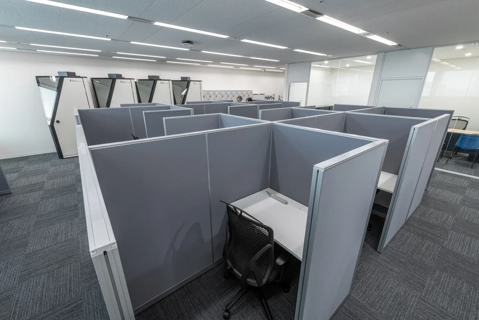 複数のグレーのパーティションで区切られたデスクと椅子が並ぶオフィス空間