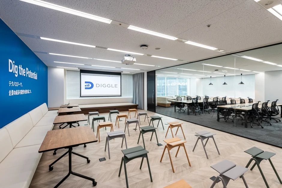 「Dig the Potential」のメッセージと「DIGGLE」のロゴが映るスクリーンが特徴のモダンなオフィス空間