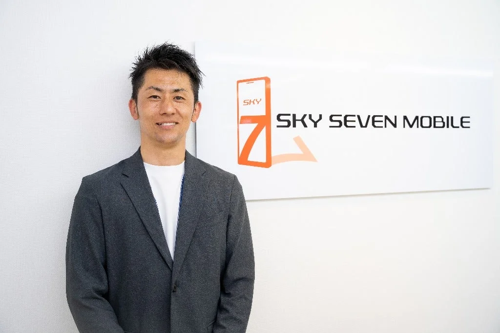 SKY SEVEN MOBILEロゴの前で笑顔の男性