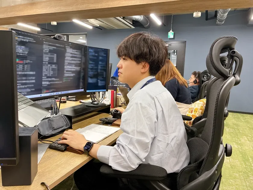 オフィスで複数のモニターを見ながら作業する若い男性の様子