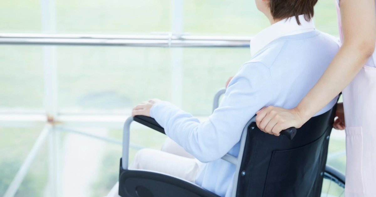 看護師が車椅子に乗った人を押し、窓の外を眺めている様子