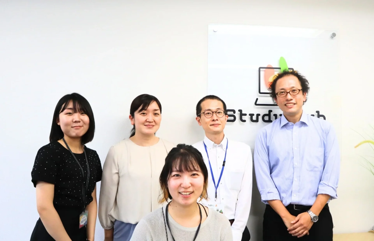 オフィスで「Study web」のロゴを背景に、5人の男女が笑顔でポーズをとっている集合写真です。和やかな職場の雰囲気が伝わります。