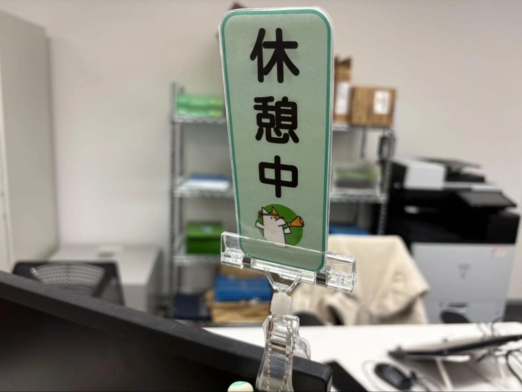 オフィスと思われる場所で、「休憩中」と書かれた立て札がデスクに置かれています。かわいらしいキャラクターのイラストも描かれています。