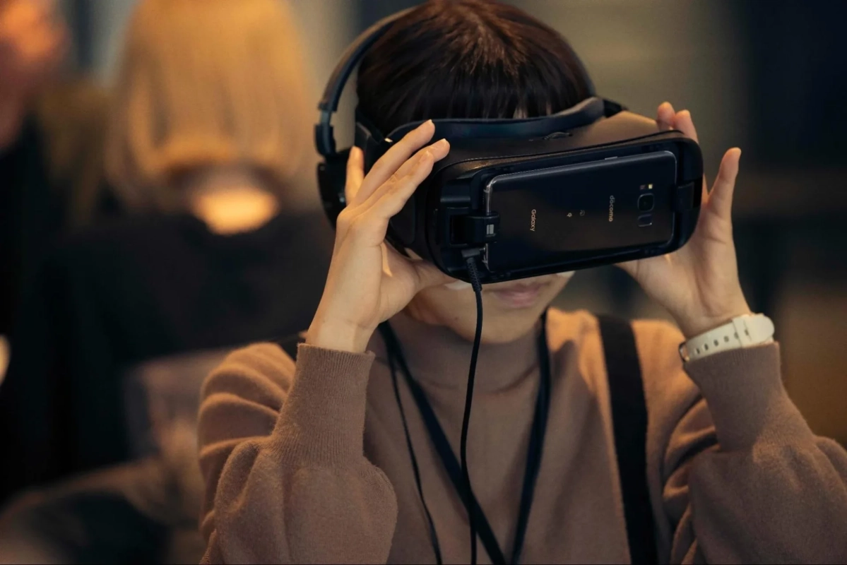 一人の人物がVRヘッドセットを装着し、スマートフォンをセットして仮想現実の世界を体験している様子です。ヘッドホンも着用しており、没入感のある体験をしていることが伺えます。