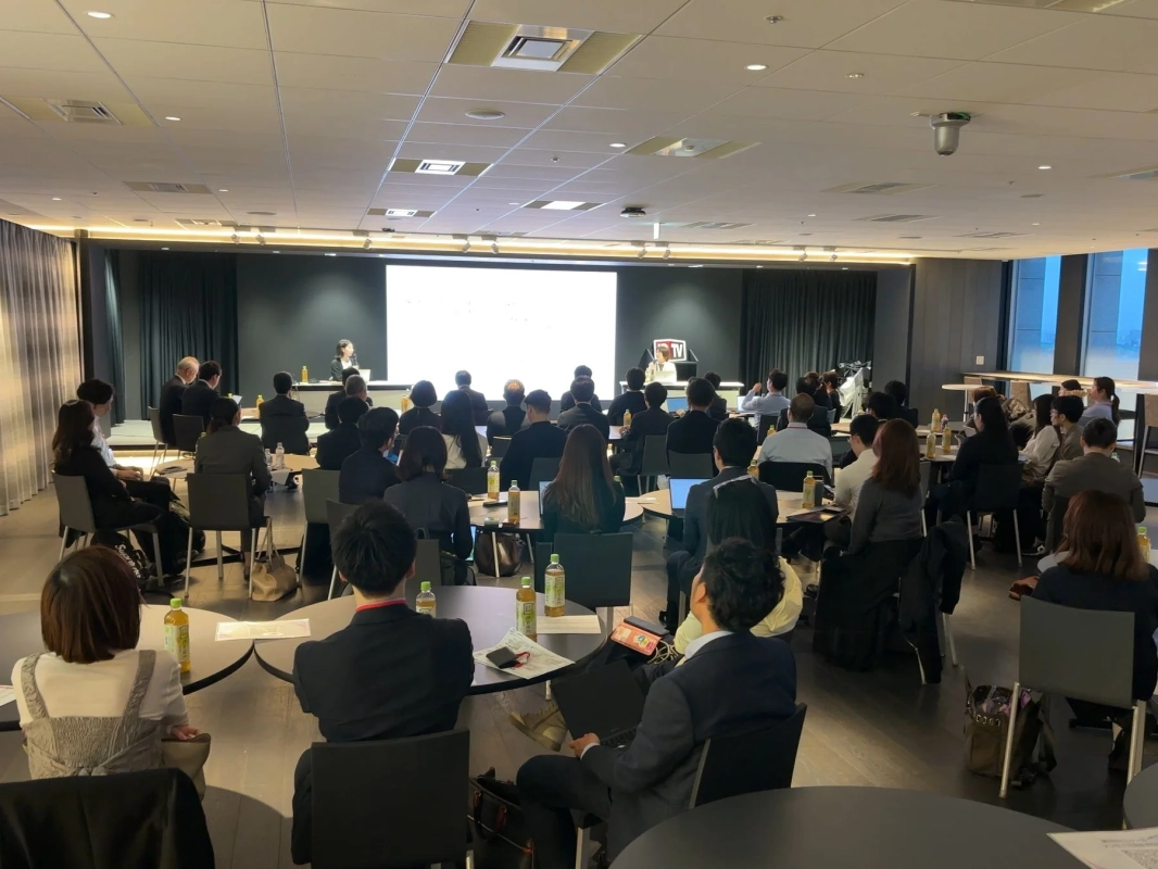会議室で多くの参加者がセミナーまたはプレゼンテーションを聴講している様子です。