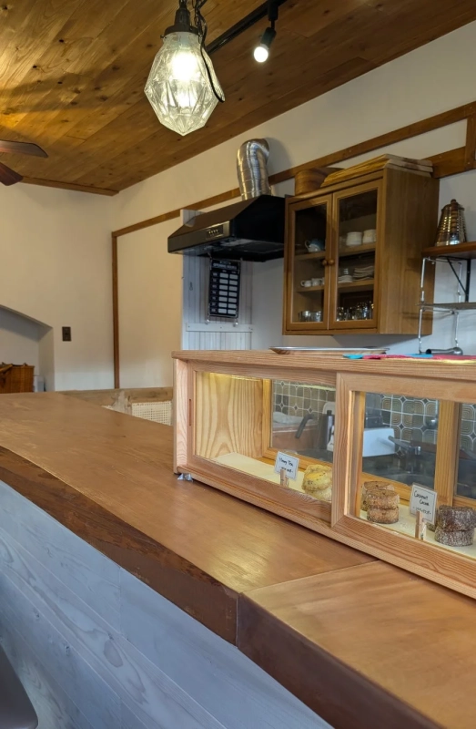 木製のカウンターが特徴のカフェの店内風景。カウンター上にはハニーティーとココナッツココアのスコーンが入ったショーケースがあり、温かみのある照明が空間を演出しています。