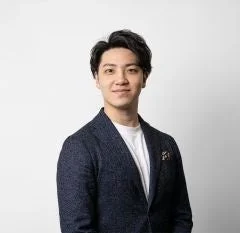 紺色のブレザーと白いTシャツを着用し、カメラに向かって穏やかに微笑んでいる若いアジア人男性のポートレート
