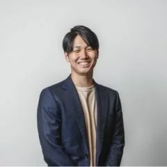 紺色のジャケットとベージュのTシャツを着用した若い日本人男性