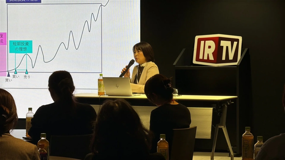 投資セミナーで女性がマイクを手に講演している場面。