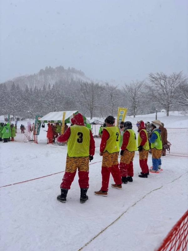 雪が降る中、虎柄のパンツと赤い服に黄色のゼッケンをつけた人々が雪原に集まっています