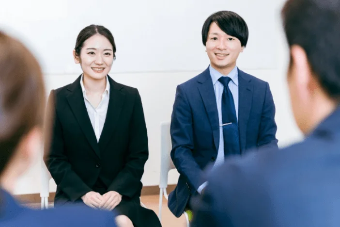 ビジネススーツを着た男女2人が、笑顔で座って話を聞いている様子