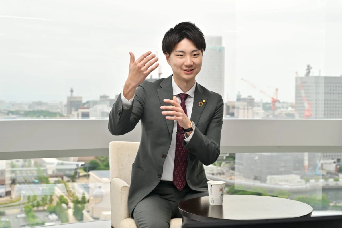 スーツ姿の若い男性が笑顔で身振り手振りを交えながら話しています。