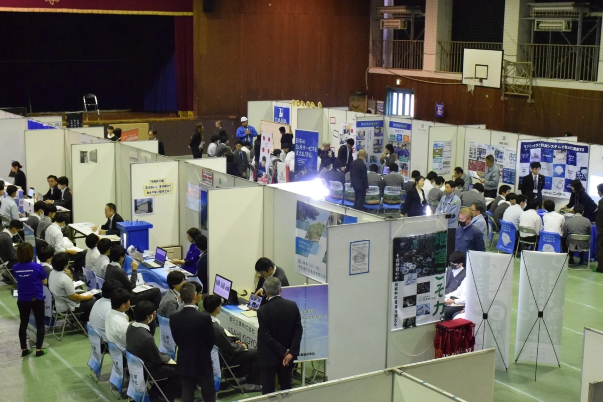 就職説明会のような会場で多くの企業ブースが出展し、参加者と企業担当者が活発に交流する様子