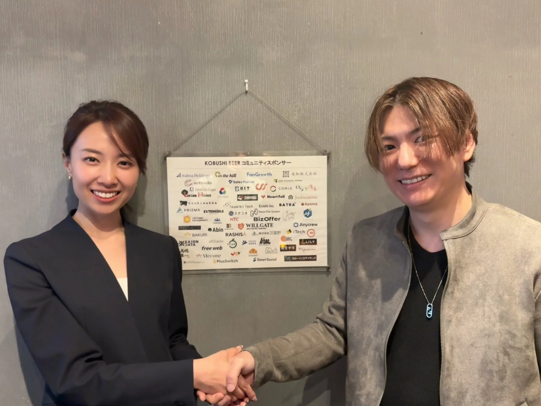 笑顔で握手する男女と企業ロゴのボード