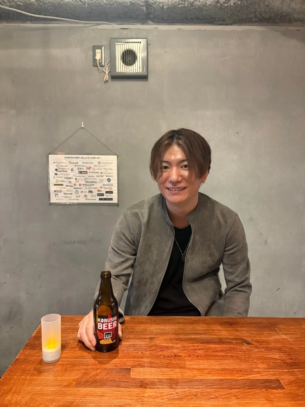 笑顔でKOBUSHI BEERのボトルを持つ男性
