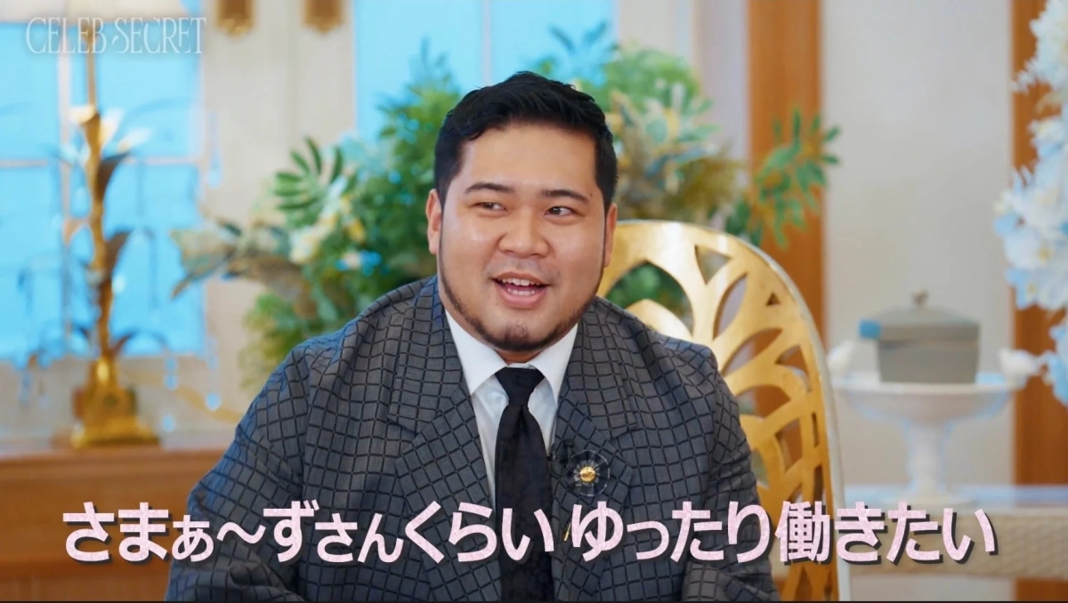 patterned suit and tie is smiling and speaking in what appears to be an interview setting
