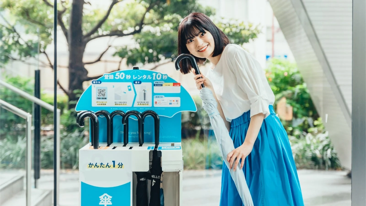 笑顔の女性が傘シェアリングサービスの前で傘を手にしている