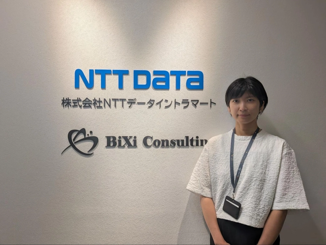 NTT Dataと株式会社NTTデータイントラマート、BiXi Consultingのロゴが描かれた壁の前に立つ女性