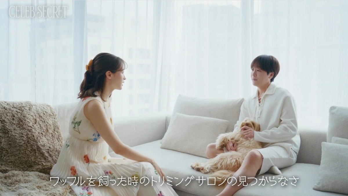 明るいリビングで、ソファに座る男女が犬を抱きながら会話している様子