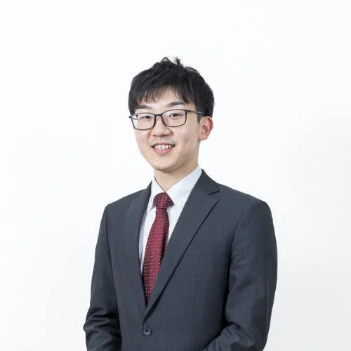 眼鏡をかけた若いアジア人男性が穏やかに微笑んでいるポートレート写真