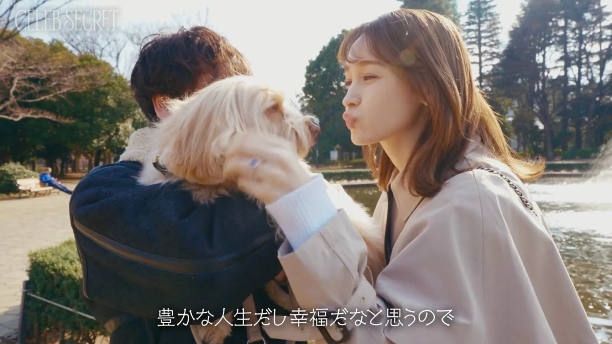 公園で、男性が抱っこしている犬に女性がキスをしようとしている瞬間の画像