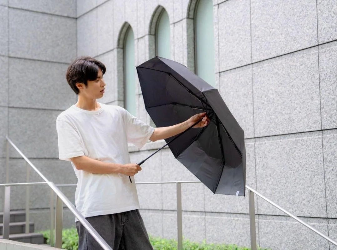 屋外で黒い傘を操作する若い男性