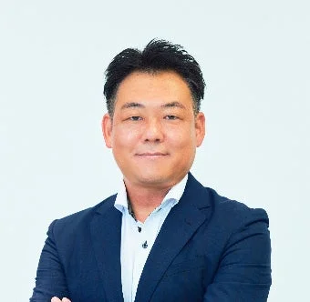 白い背景の前で、ダークスーツを着たアジア人男性がわずかに微笑んでいる上半身のポートレート写真