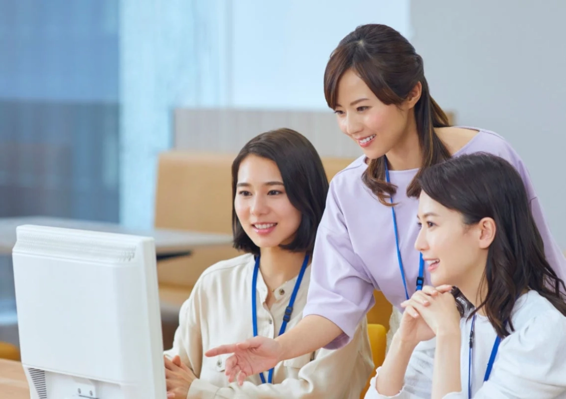 オフィスで女性たちがPC画面を見ながら協力し合う様子