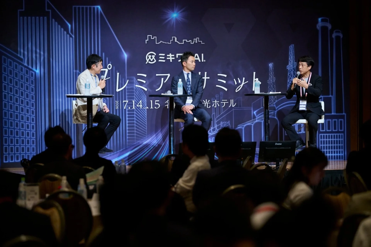 「ミキワAI プレミアサミット」というイベントで、3人の男性が壇上でパネルディスカッションを行っています。背景には未来的な都市のシルエットが描かれ、聴衆が熱心に耳を傾けている様子が伺えます。